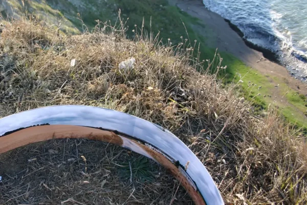 El anillo apoyado en el borde del acantilado, entre hierba seca; abajo, la playa y el mar rompiendo contra la roca.