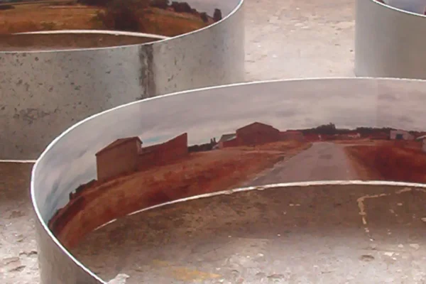 Vista cenital de un anillo grande: en su interior, un caserío de construcciones bajas de ladrillo y una carretera cruzando campos arados de tierra rojiza.