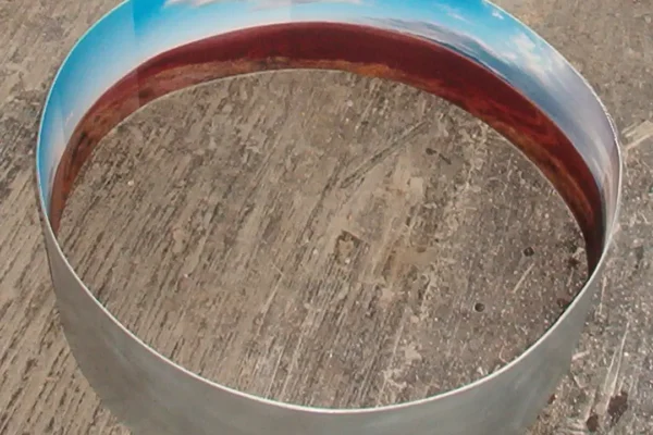 Un solo anillo sobre el hormigón rayado del taller; la franja interior lleva el cielo arriba y la tierra roja abajo, mientras el exterior queda en zinc desnudo.